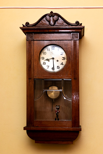 Antique wall wooden clock with hands of the clock and gold pendulum