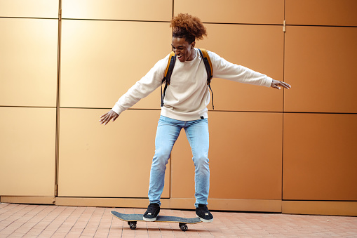 An urban young African American man on a skateboard. in front of the orange wall