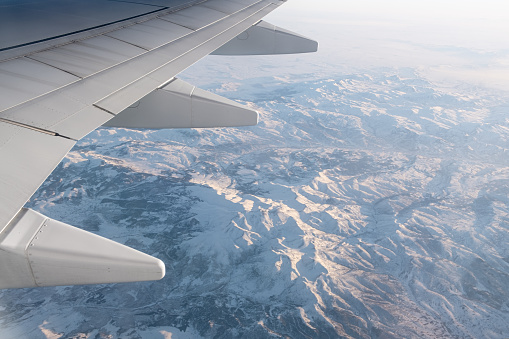 aerial snow covered mountain ridge peaks in alps at winter, above view airplane wing