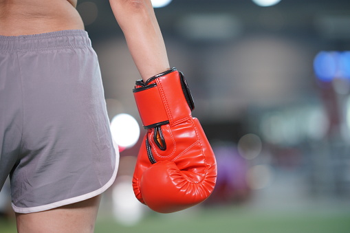 Close up of red boxing glove in woman right hand standing, turning back with part of body and copy space.