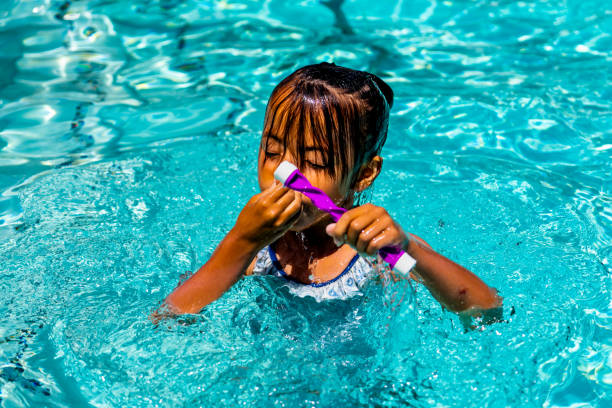 con el calor del sol abrazándola, una niña, de unos 7 años, encuentra puro deleite en una piscina en un día de verano. sus salpicaduras juguetonas y risas llenan el aire mientras se involucra con una batuta de buceo. - 7 10 years fotografías e imágenes de stock