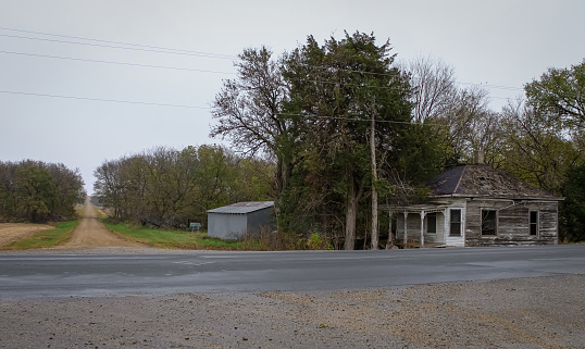 An old clapboard farmhouse stands abandoned. Front porch is gone, foundation is brick and many of the roof shingles are blown away. The small farm way of life seems to have blown away too.