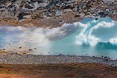 Abstract nature background with sunlight through clouds reflected in turquoise mountain lake mirror. Beautiful pure alpine lake with cloudy sky reflection among vivid autumn colors in high mountains.