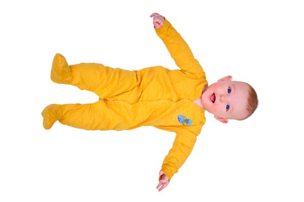 un bebé feliz acostado en una alfombra de juego en pijama amarillo, vista superior, aislado sobre un fondo blanco. niño sonriente de cuerpo entero en piso blanco, espacio de copia. niño de seis meses - animal egg eggs basket yellow fotografías e imágenes de stock