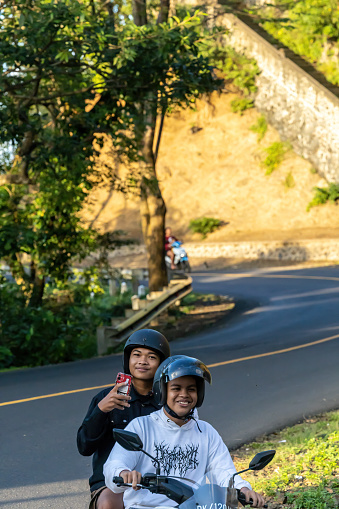 Bali, Indonesia May 13, 2023 Scooter drivers in traffic on a windy road.