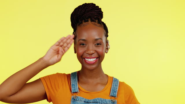 Salute, portrait and black woman with deaf hearing aid in greeting sign language isolated in a yellow studio background. Smile, welcome and young female with a listening disability doing hand gesture