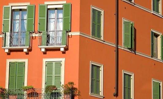 Close up on an orange building with green window shutters, geometric lines, bright colors, sunny day