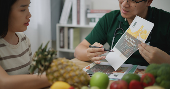 Professional nutritionist asian man consulting young woman in clinic or hospital, He explain about proportion of fruits and vegetables on paper for good healthy, correct nutrition and diet concept