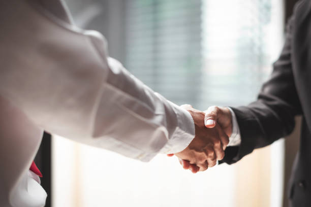 Close up of two business people shaking hands while sitting at the working place stock photo