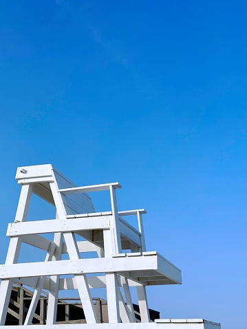 Empty white painted lifeguard tower on a sunny day in front of a blue sky