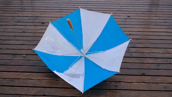 A blue and white umbrella placed on a wooden plank floor