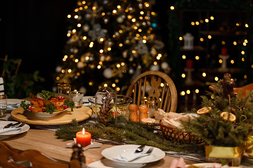 Selective focus shot of glistening Christmas lights in the background, behind a rustic dining table set for a Christmas dinner party.