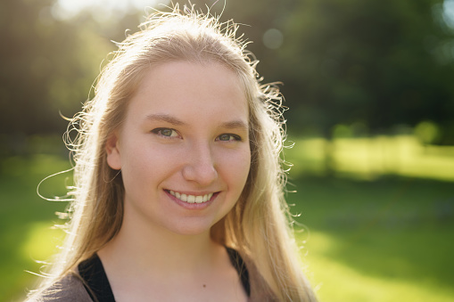 teen girl smiling in green park in sunny summer evening, lifestyle portrait