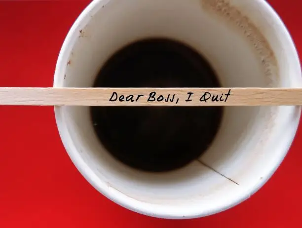 Wood coffee stirer with text written DEAR BOSS I QUIT on papay coffee cup, refers to decision making to quit job, to sign from being full time employees, voluntarily leaving job to find work life balance after pandemic