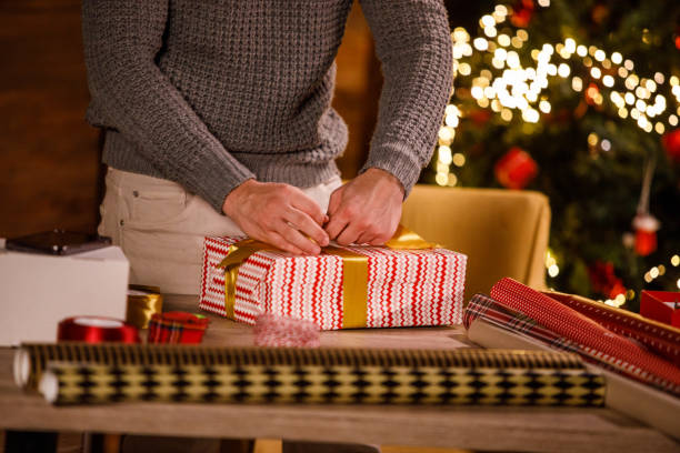 istock Young man wrapping a gold colored ribbon around a Christmas gift that he is wrapping and decorating 1498868356