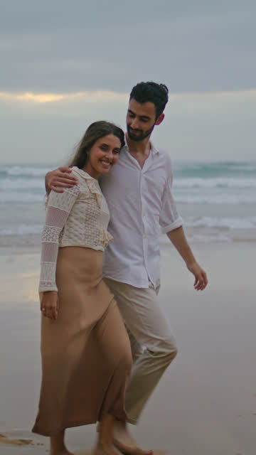 Loving couple going evening sea shore vertical. Married people embracing ocean