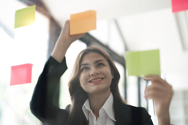 istock Asian businesswoman creating project plan on office wall with paper notes. Financial and Marketing projects 1498874936