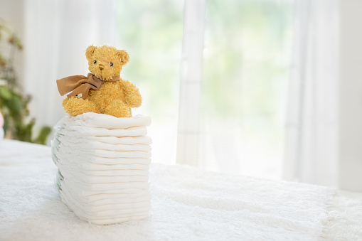 Baby diapers stack cute teddy bear sitting on top. Newborn nappies concept