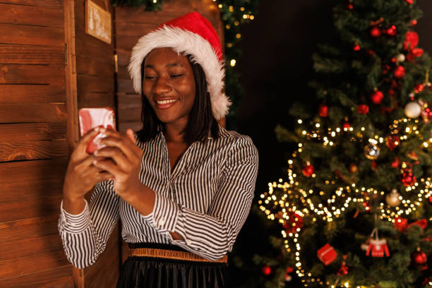 istock Young woman standing by the Christmas tree and using smart phone 1498876014