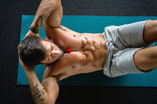 Top view of a strong man doing crunches on a mat in a gym