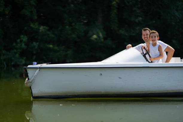 happy father and son driving electric boat on lake in summer smiling at camera together