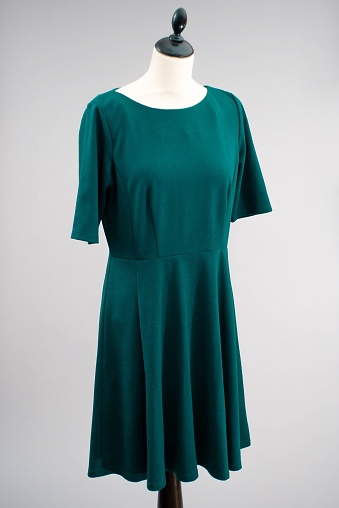 A dark green summer dress hanging on a mannequin on white background
