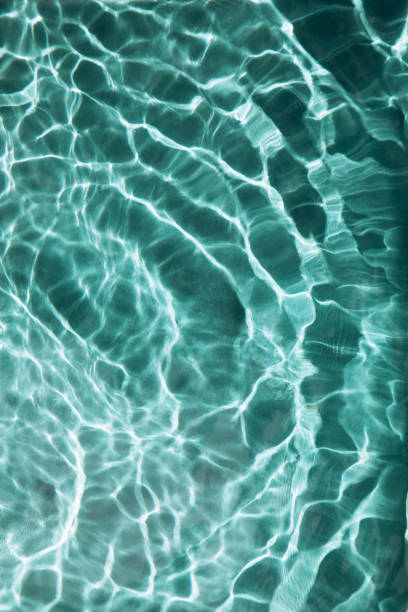 Abstract textured background, water waves in the pool with sun reflection, clear green water stock photo