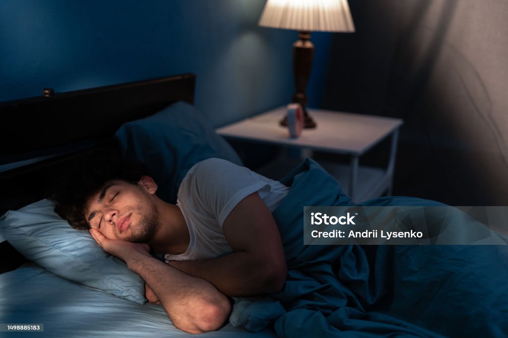 Peaceful young man sleeping in a comfortable bed alone at home, enjoying his orthopedic mattress and cozy pillow. Good sleep concept. Peaceful young man sleeping in a comfortable bed alone at home, enjoying his orthopedic mattress and cozy pillow. Good sleep concept. Copy space Sleeping Stock Photo