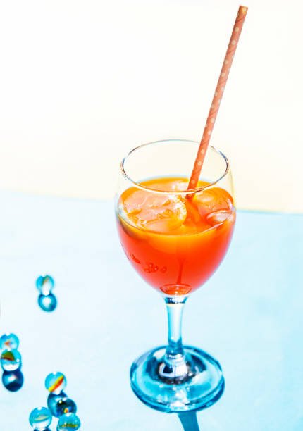 青白い背景にオレンジ色のカクテルとオレンジ色のカクテルと小さなガラス球 - drink umbrella cocktail glass isolated ストックフォトと画像