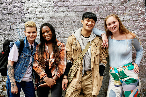 Front view of casually dressed adults leaning against painted brick wall and smiling at camera.