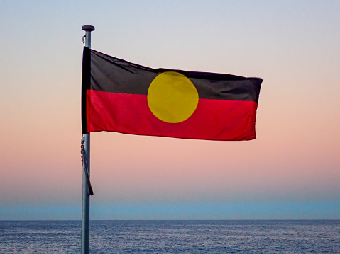 The Australian Aboriginal flag flies at Bondi Beach, Sydney at sunset in winter on 16 June 2023.  In the background is the Pacific Ocean.