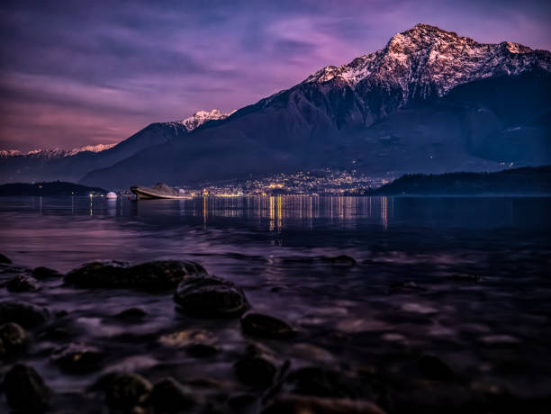 view of Lake Como between high mountains green trees with rocks on the shore and calm autumn waters a spectacular sunset between the peaks of the Alps and Lake Como in Italy