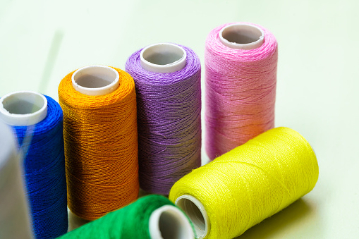 The multi-colored spools of thread lie in a row diagonally. A repeating pattern. Sewing thread texture. Hard light. Beautiful sewing items.