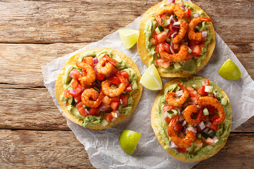 Crispy tostadas topped with guacamole, spiced shrimp, and fresh salsa closeup on the wooden table. Horizontal top view from above