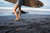 Foots of woman with surf board walking on black sand before serfing. Beach travel in Sri Lanka