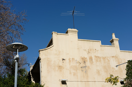Close-up on a side wall of a building with chimney, antenna, street light, and deep blue sky beyond.