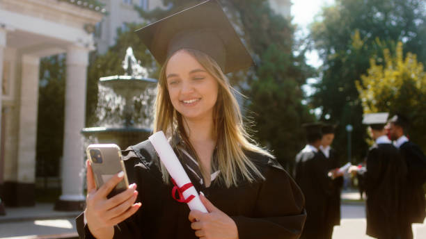 istock Smiling large cute lady student take the smartphone she make a video for her parents after she was graduate in the college garden background other group of multiracial students discussing all together 1498908202