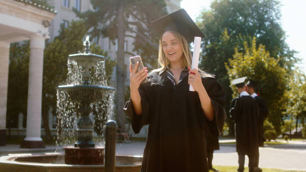 istock Pretty young lady student graduate called her parents on the camera using the smartphone she discussing very excited holding her diploma in the college garden 1498908310
