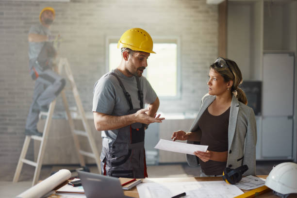 istock Female inspector and manual worker talking about plans at renovating home. 1498909795