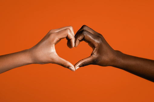 Diverse hands making a heart symbol against orange background