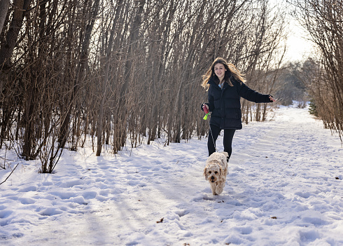 Teenage girl walking her dog in the winter park in Canada