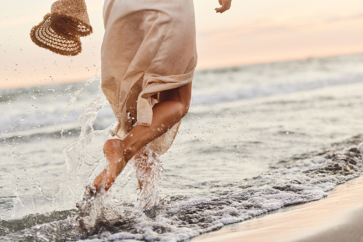 Rear view of unrecognizable woman in a dress having fun while running through sea on the beach. Copy space.