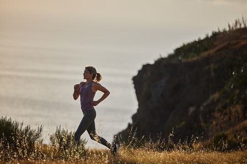 Determined female athlete running on a cliff by the sea in summer day. Copy space.