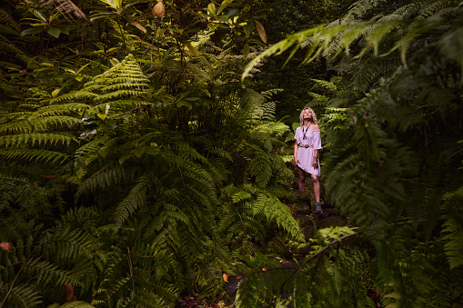 Carefree woman day dreaming while standing in lush foliage at the forest.