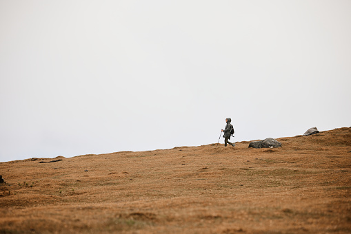 Young female hiker in raincoat walking on a mountain during bad weather conditions. Copy space.