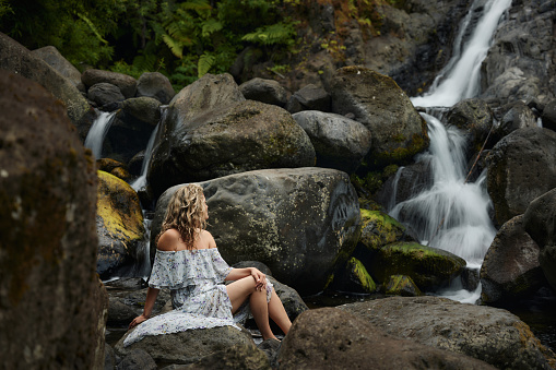 Young woman relaxing on the rocks by the waterfall.