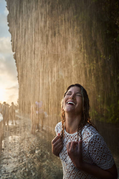 Carefree woman having fun while standing under the waterfall with her eyes closed.