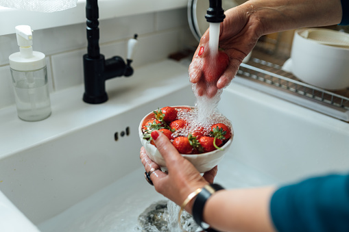 Woman’s hands washing strawberries in the kitchen sink