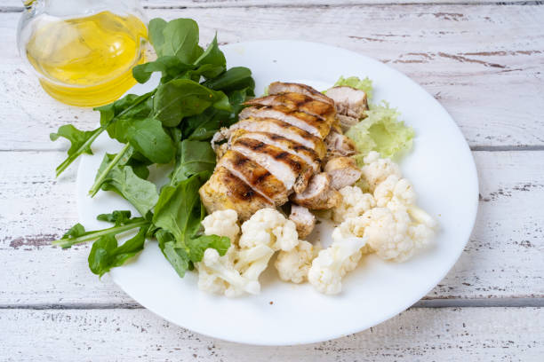 grilled chicken breast with cauliflower and arugula served in a white plate.