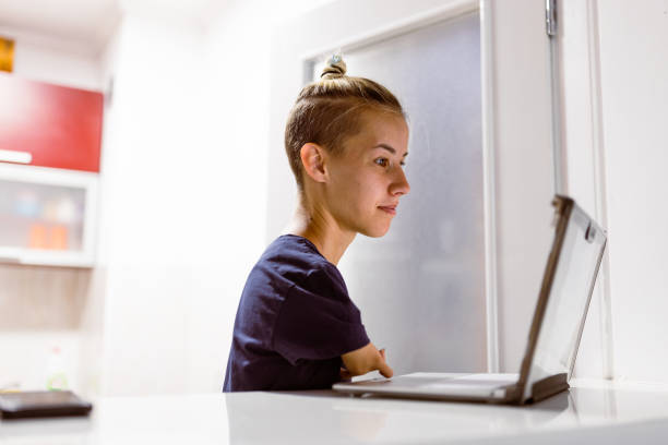 Limitless Potential: Embracing Remote Work with Passion and Perseverance of young woman with disability Remarkable young woman with a disability confidently working from home. With her laptop open before her, she tackles her tasks with determination and focus. adaptable workplace stock pictures, royalty-free photos & images